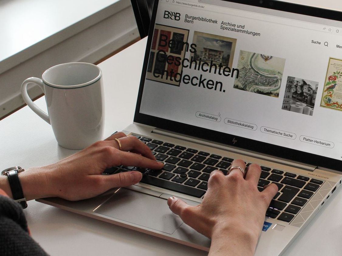Eine Person, welche die Webseite der Burgerbibliothek Bern an einem Laptop besucht.