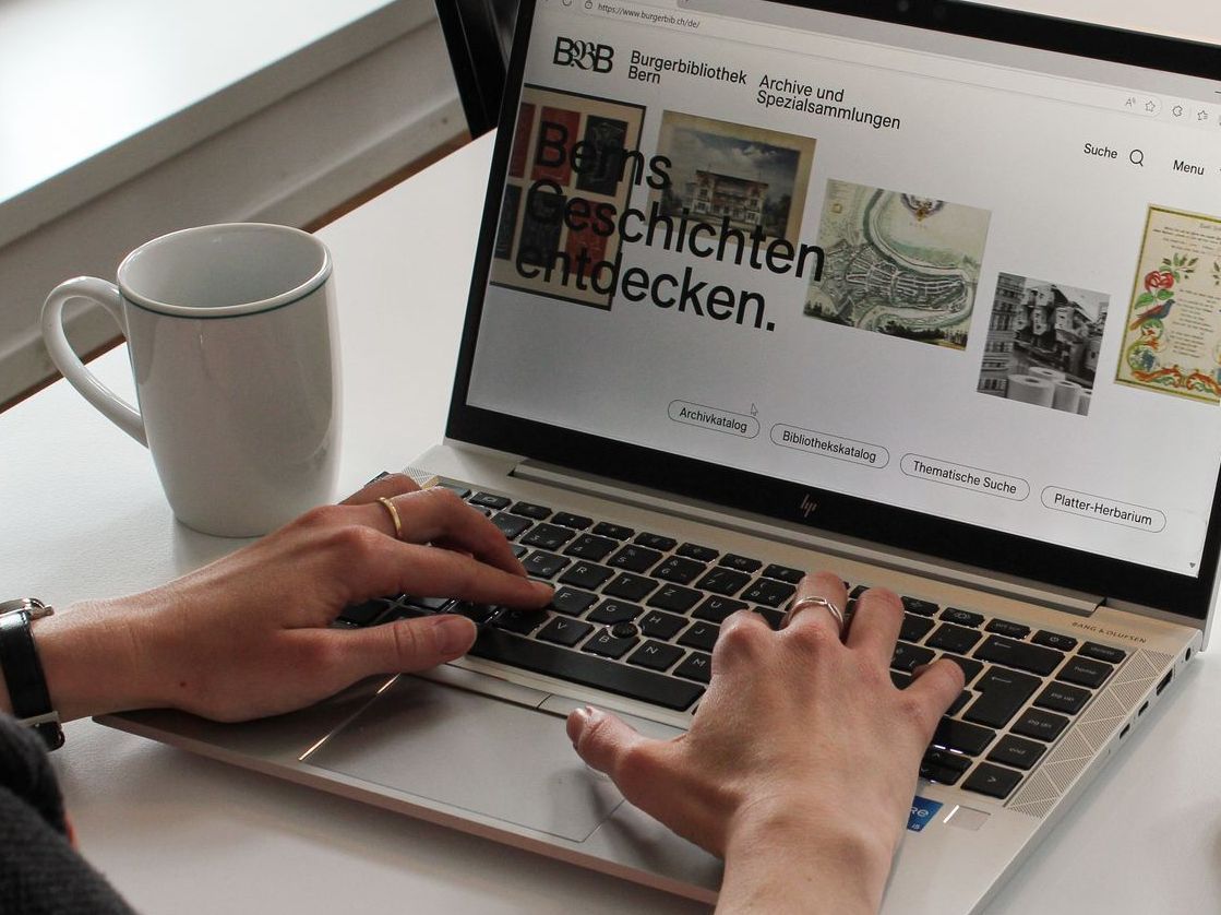 Eine Person, welche die Webseite der Burgerbibliothek Bern an einem Laptop besucht.