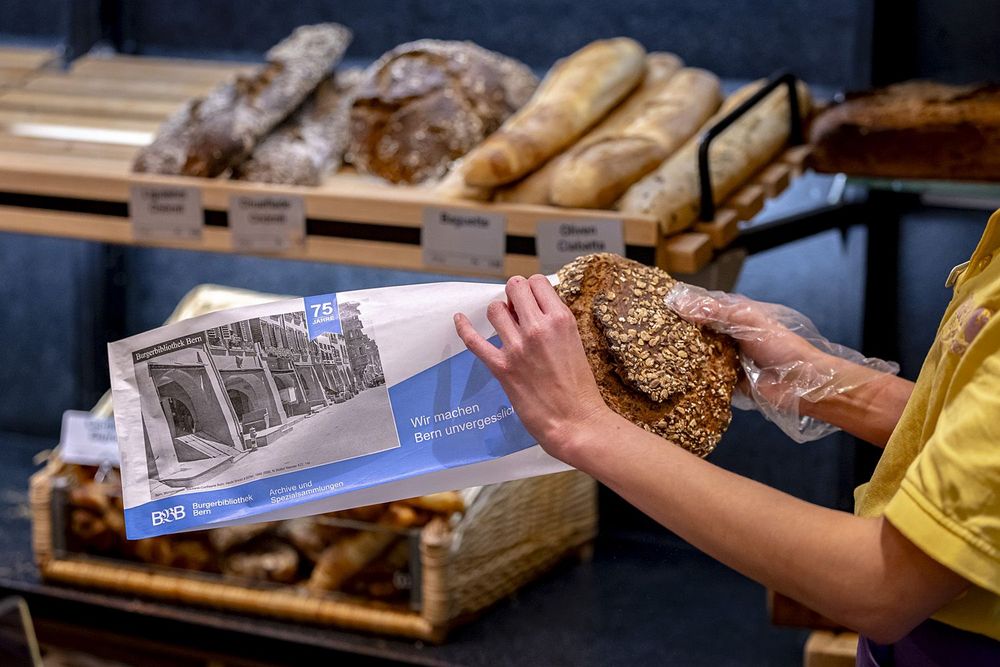 Fotografie zeigt eine Mitarbeiterin der Bäckerei, welche ein Brot in ein Brotsack steckt.