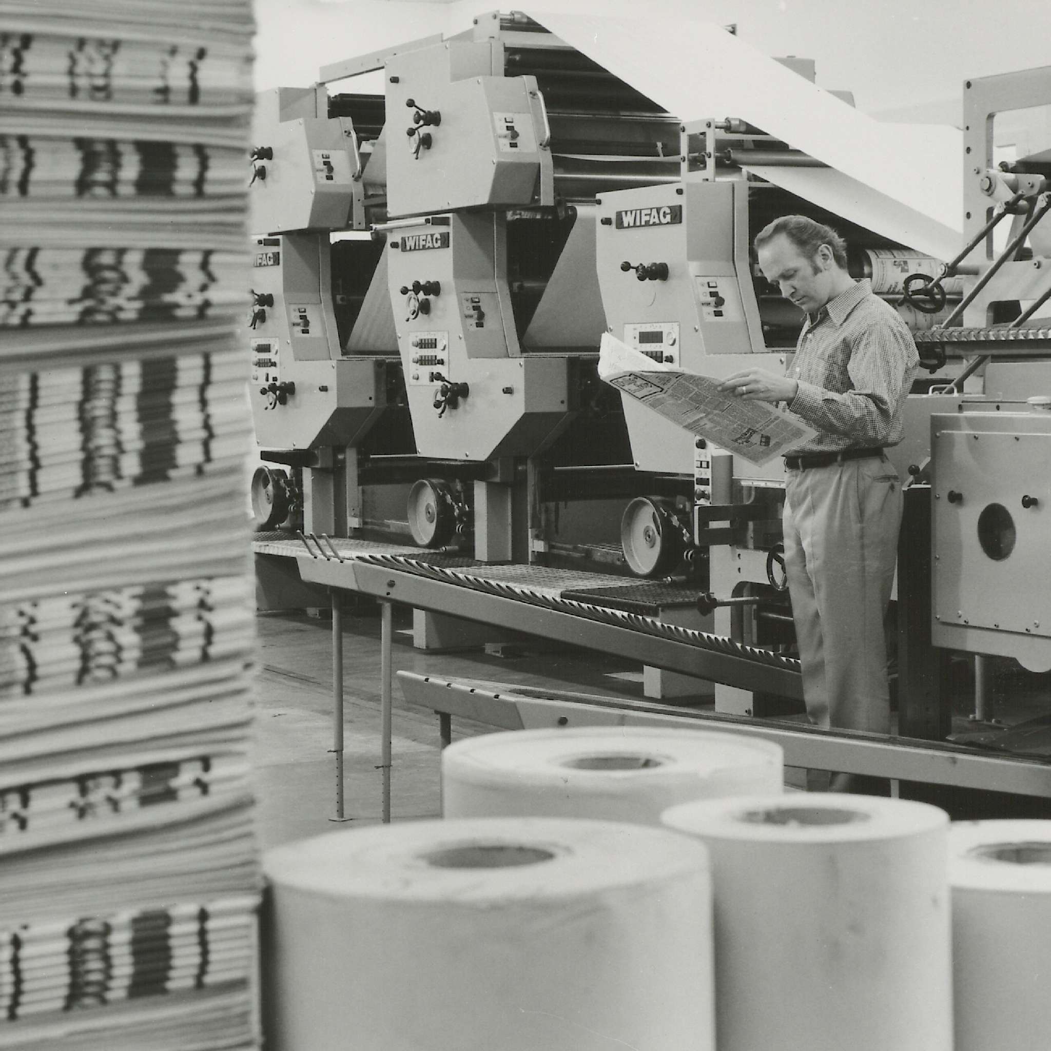 Mann steht vor einer Offsetdruckmaschine und kontrolliert das Druckerzeugniss. Fotografie aus dem Archiv FI WIFAG.